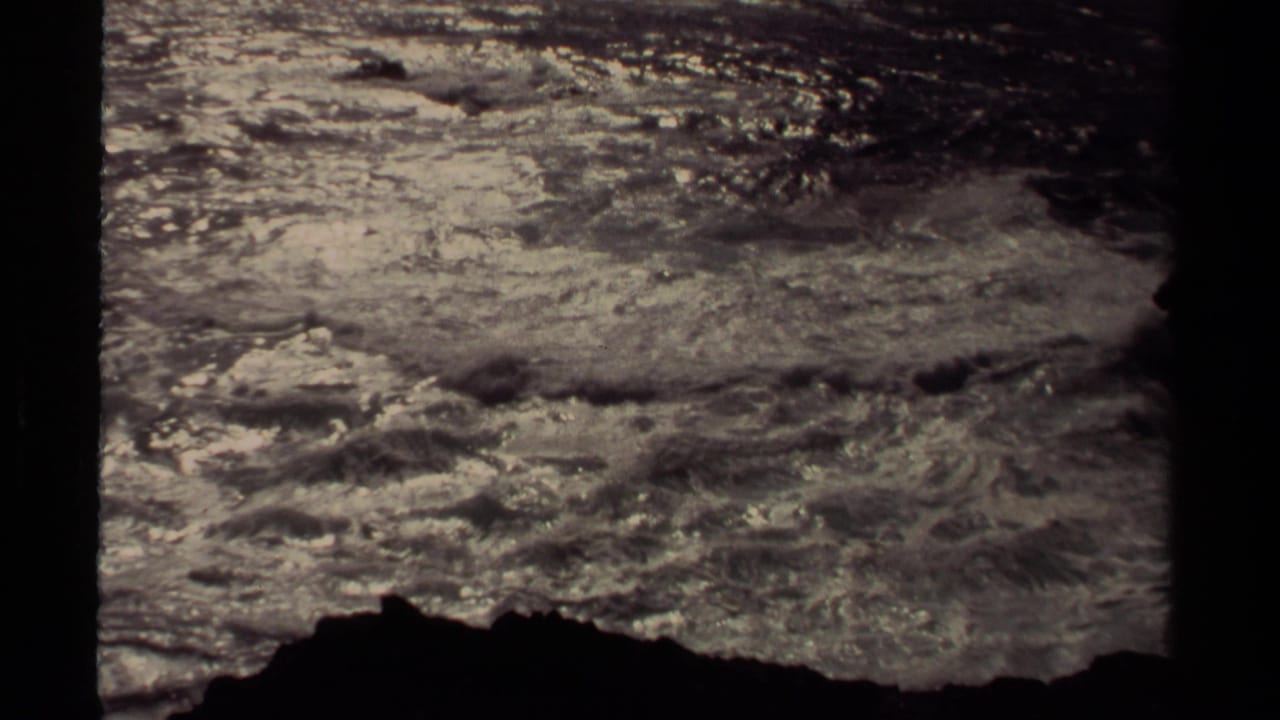 White surf spreads across the water above a dark rocky shoreline silhouette.