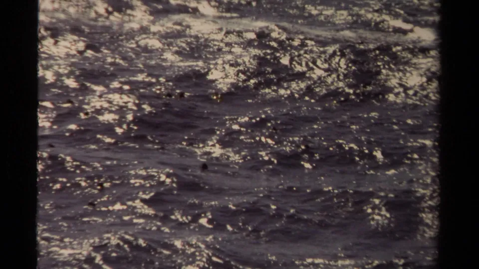 Grainy 1980 8mm frame of churning water in Mendocino, with bright shimmer and darker current areas.