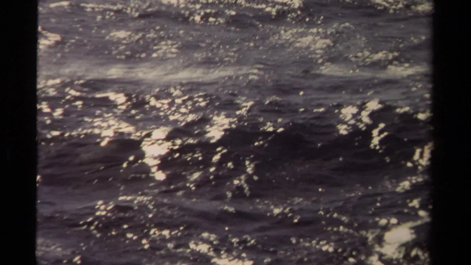 Mendocino 1980 home-movie still of dark surf, white foam streaks, and uneven light across the water.
