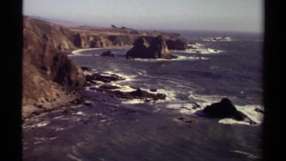Mendocino coast seen from above, with rugged cliffs, offshore rocks, white wave lines, and open Pacific water in a soft 8mm frame.