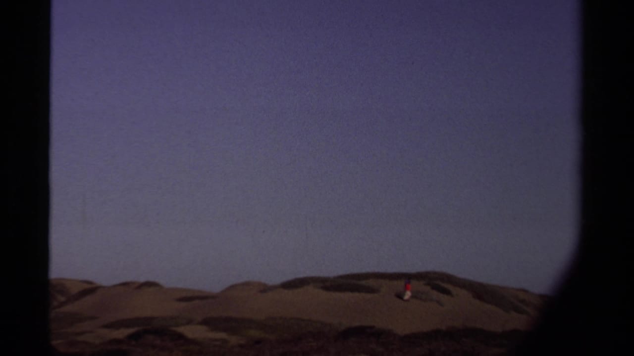 The camera holds on Mendocino dunes as a small figure in red crosses the ridge line beneath a wide sky.
