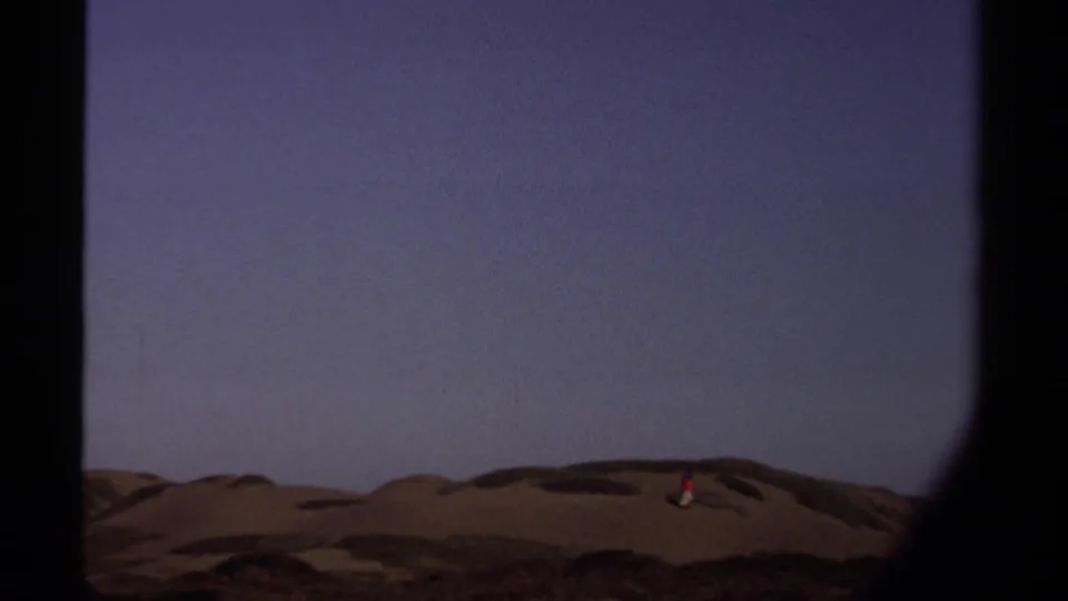 The camera holds on Mendocino dunes as a small figure in red crosses the ridge line beneath a wide sky.