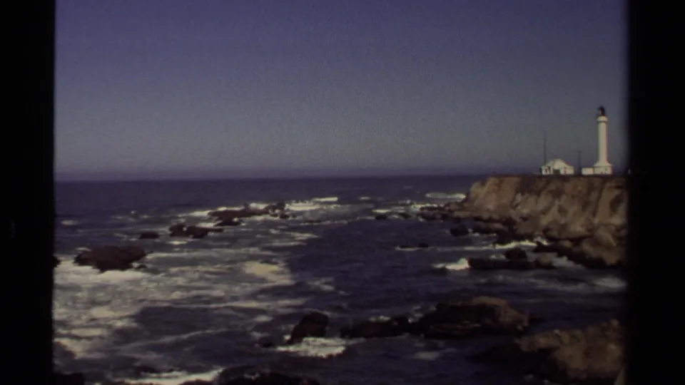 1980 8mm view of Point Arena Lighthouse above a rugged Mendocino coastline with waves breaking on dark rocks.