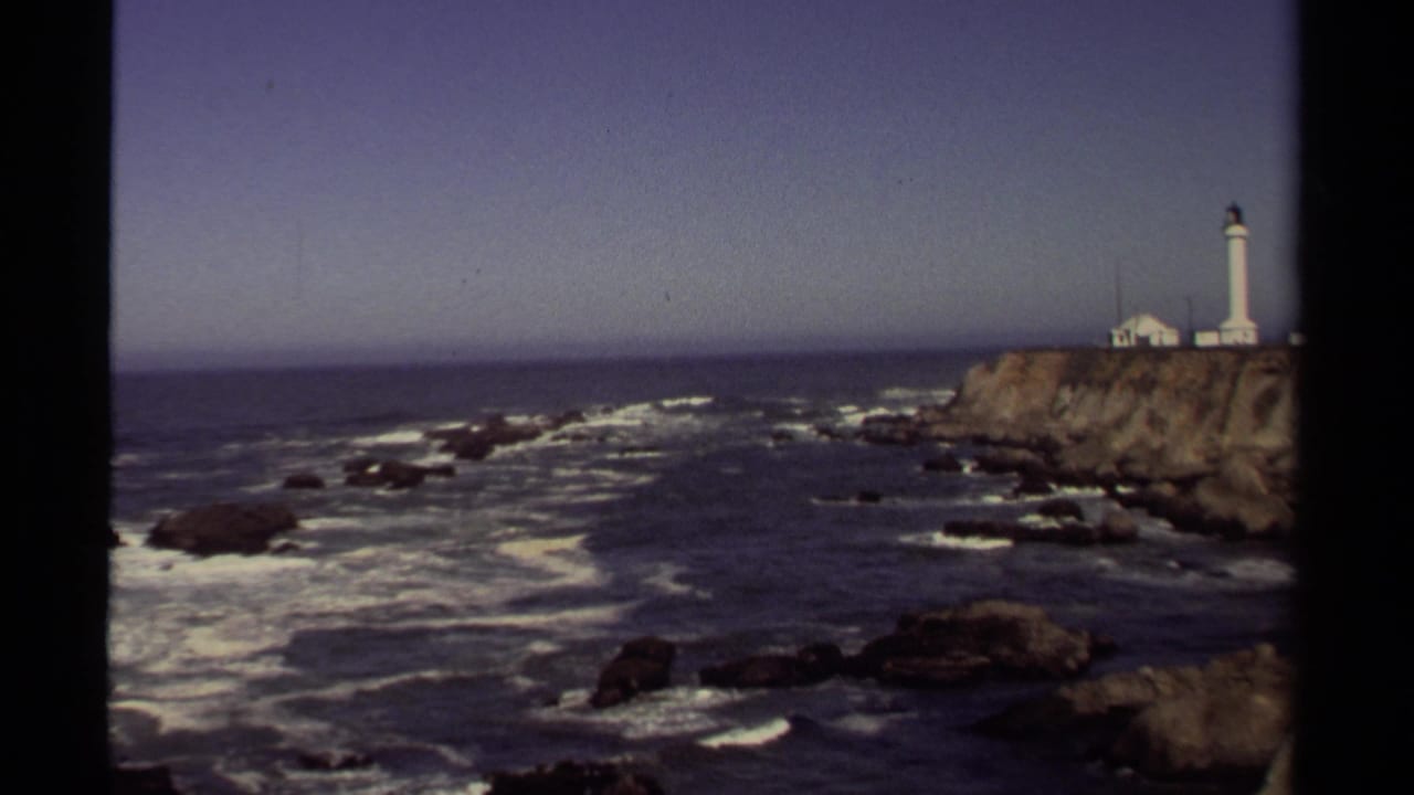 Wide coastal view with lighthouse on a rocky headland above breaking surf.