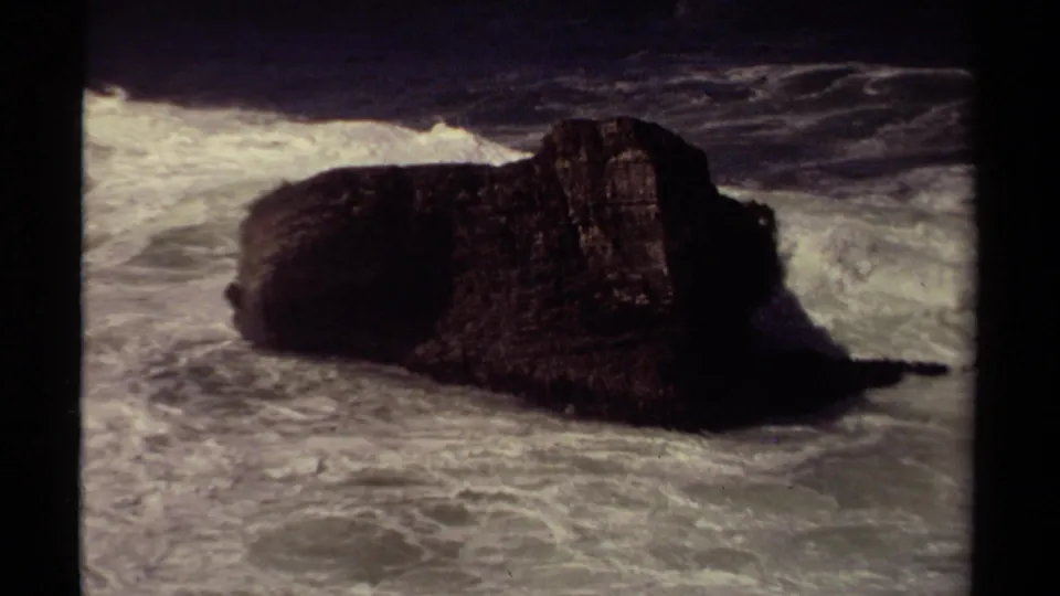 1980 Mendocino coast frame with a large dark rock framed by white breaking surf in vintage 8mm texture.