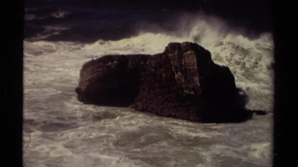 A stronger wave begins breaking behind the dark Mendocino rock, sending spray upward over the foamy water.