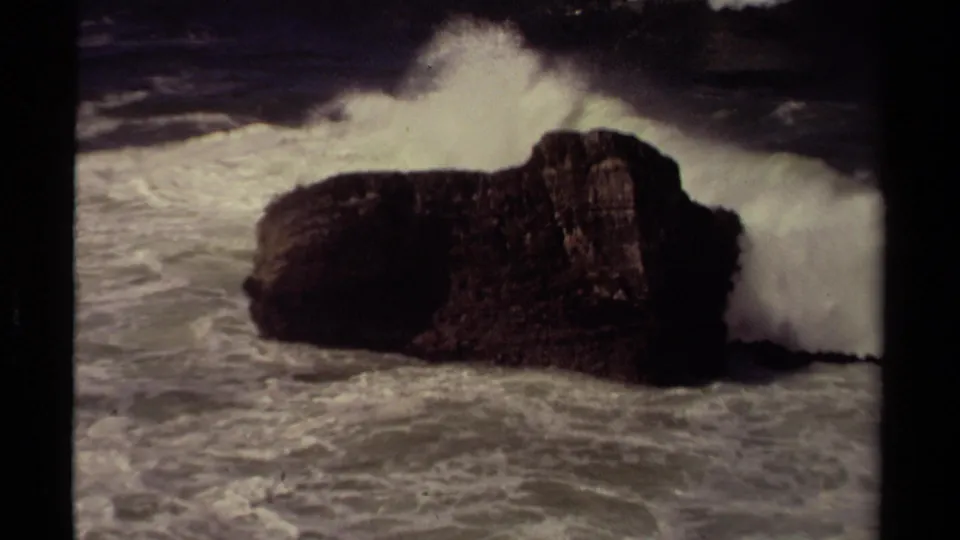 A large white wave crashes against the side of the Mendocino coastal rock in grainy 8mm footage.