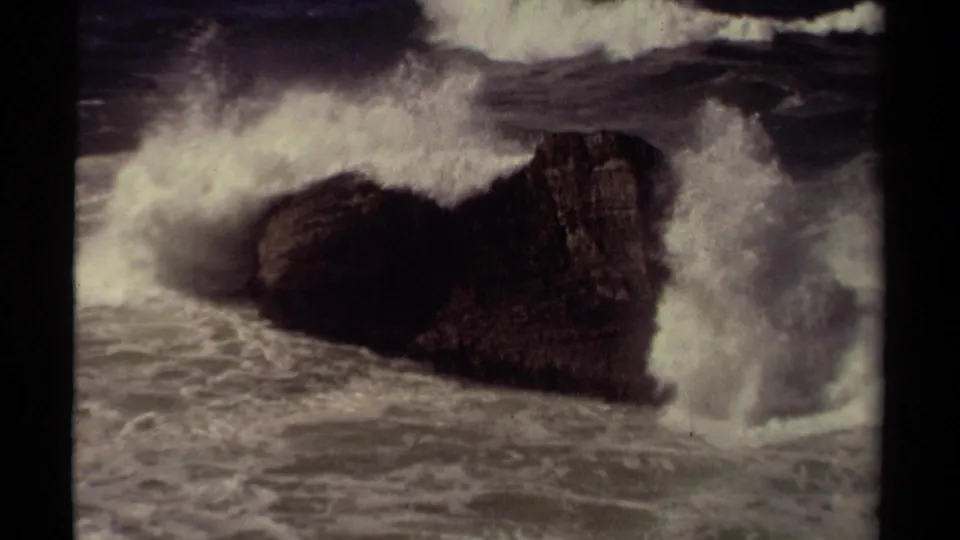 A large wave crashes around a dark rock formation on the Mendocino coast in 1980 8mm home-movie footage.