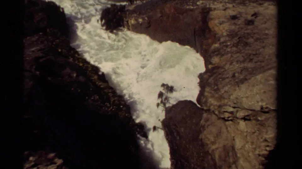 1980 Mendocino 8mm frame showing turbulent white water framed by rugged dark rocks and tan stone ledges.