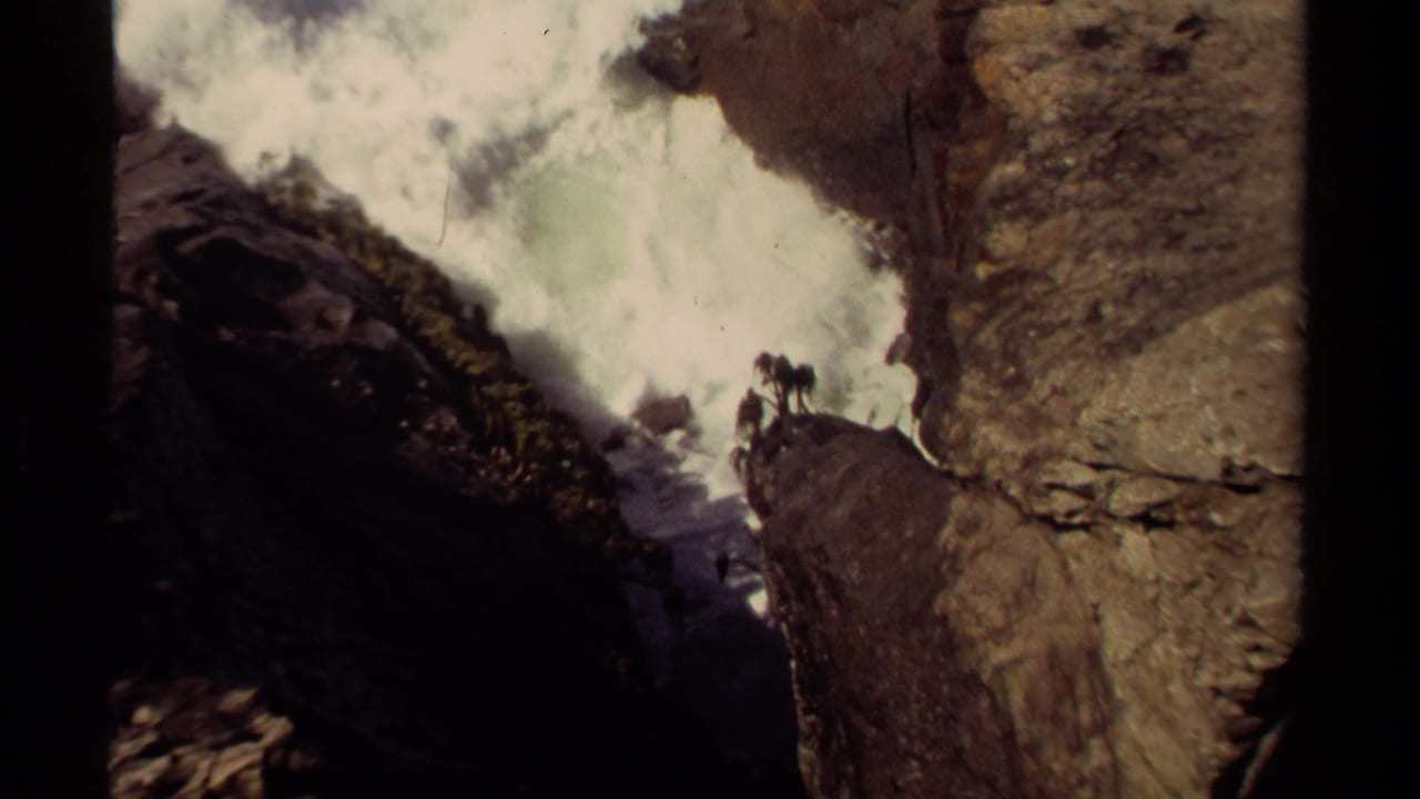 A burst of white surf breaks against rocks in a narrow coastal passage.