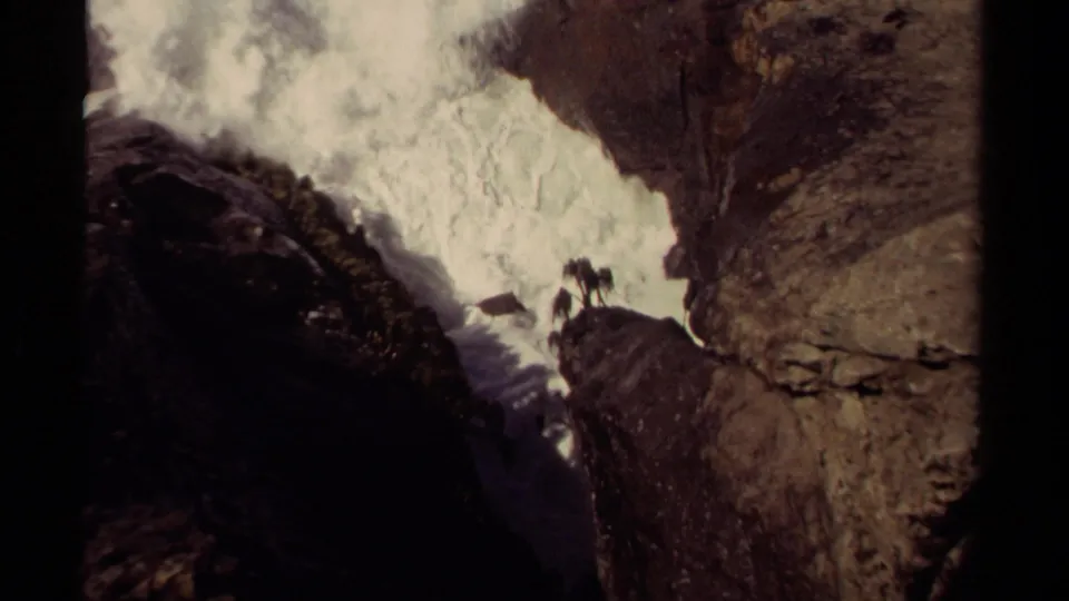 Mendocino 1980 8mm frame of surf bursting against coastal rocks, with tiny people visible in the distance.