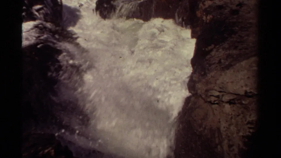 Mendocino 1980 8mm frame of pale surf spreading below rugged coastal rocks and a cliff wall.