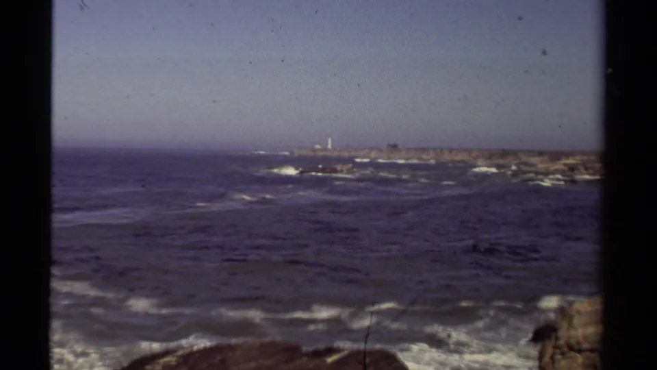 1980 Mendocino 8mm view across blue ocean toward a rocky island with a small lighthouse-like structure.