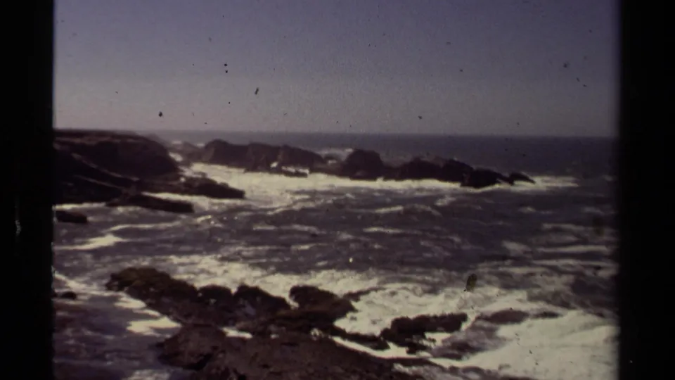 Mendocino coastal surf in 1980 home-movie footage, with foamy Pacific waves moving around jagged dark rocks.