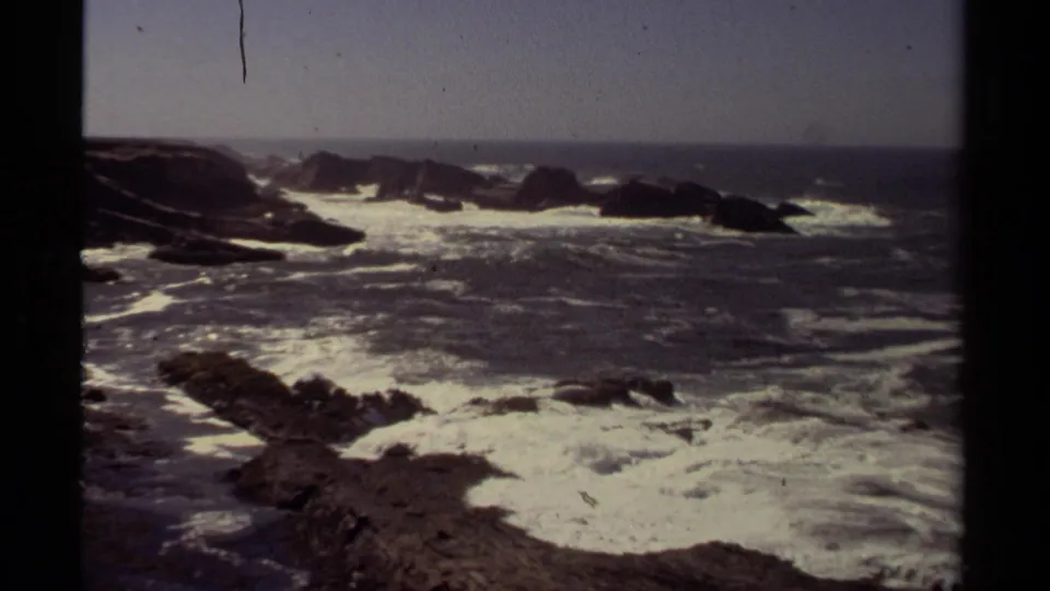 1980 8mm coastal shot from Mendocino showing heavy white surf washing over rocks beneath a calm blue-gray sky.