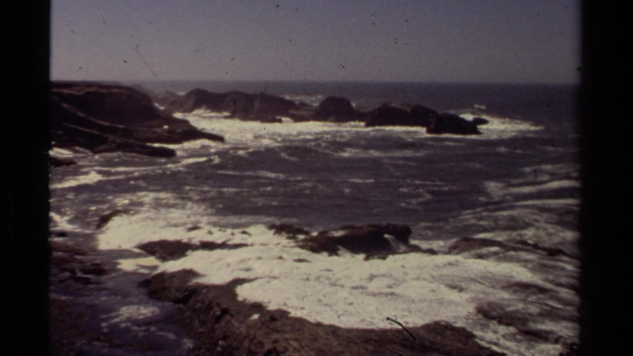 Surf spreads across rocks with offshore formations on the horizon.