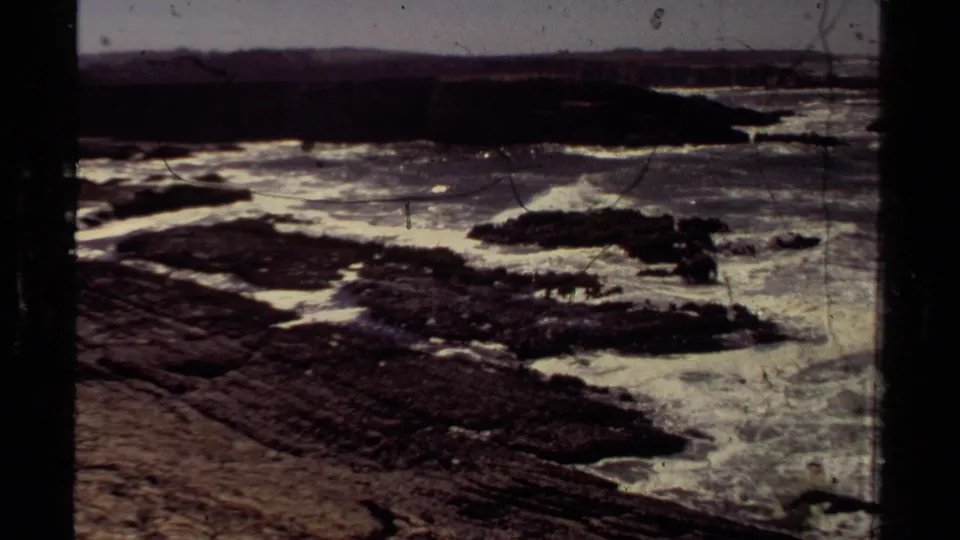1980 Mendocino 8mm view of a rocky shoreline with foamy water moving through dark coastal ledges.