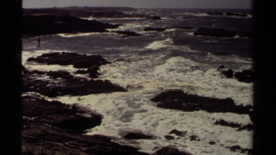 High-angle 8mm coastal view of turbulent Pacific surf crossing dark rocks near Mendocino.