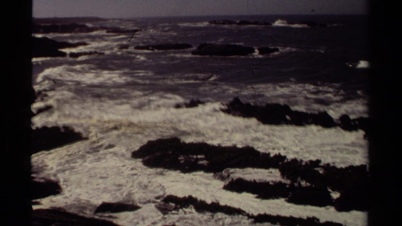 1980 Mendocino coastal frame with white surf churning over black rocks and darker ocean water in the distance.