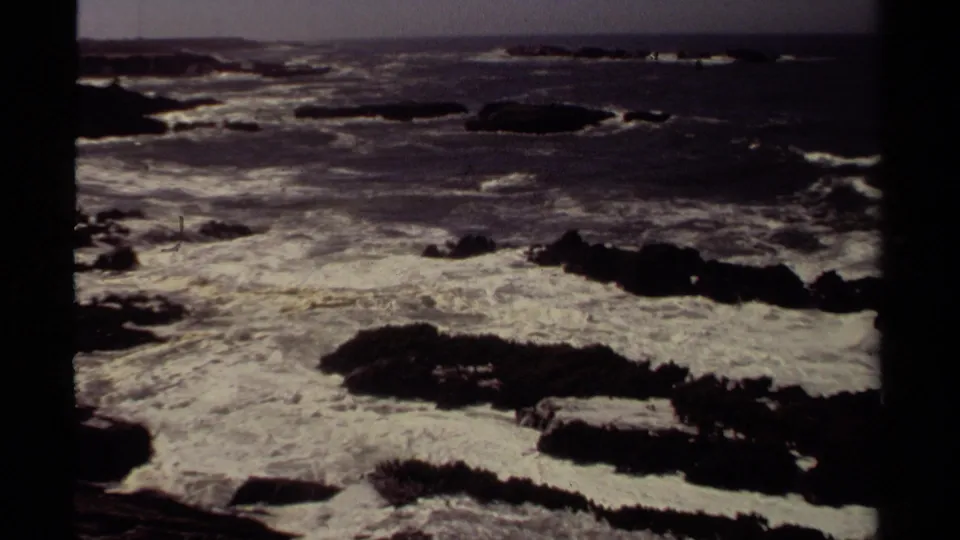 1980 Mendocino 8mm view of turbulent ocean foam washing through a field of dark shoreline rocks.
