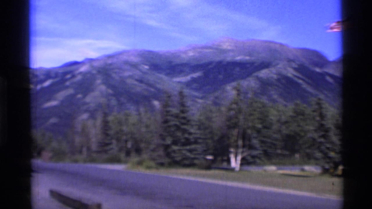 Mountain range, evergreen trees, and a roadside view seen through dark film-frame borders.