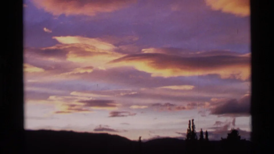 1977 Alaska 8mm frame showing layered gold and purple dusk clouds above a dark mountain ridge and tree silhouettes.