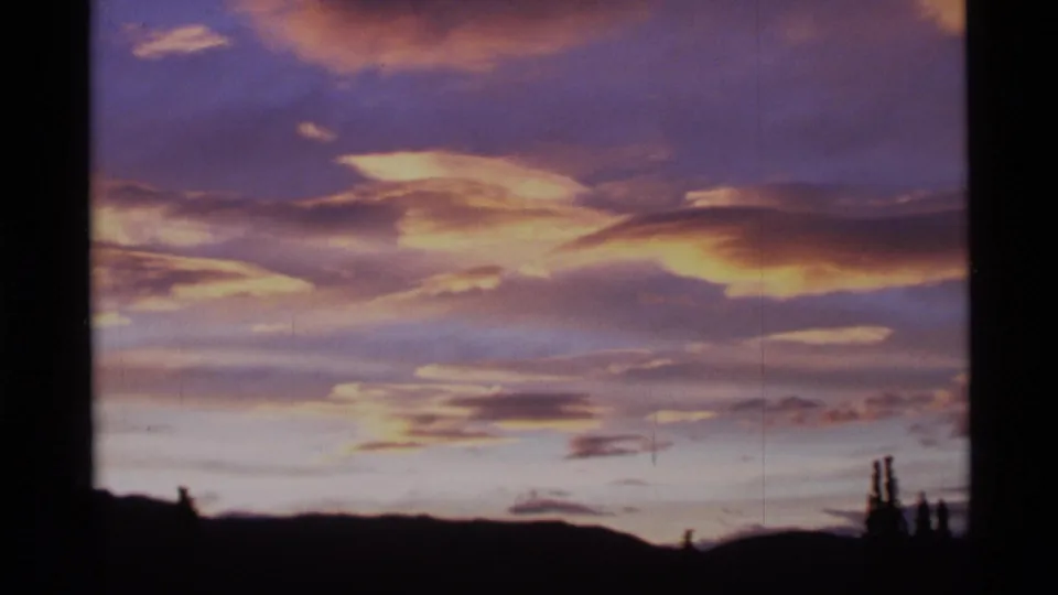1977 Alaska 8mm frame with lavender and gold clouds stretching over a dark mountain horizon and faint tree silhouettes.