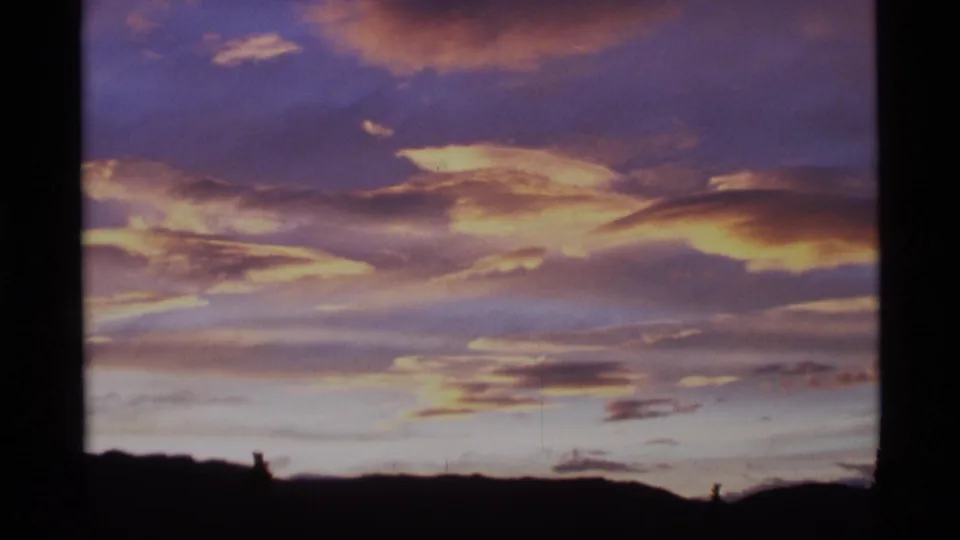 1977 Alaska 8mm frame showing warm dawn clouds against a purple-blue sky over a black silhouetted hillside.