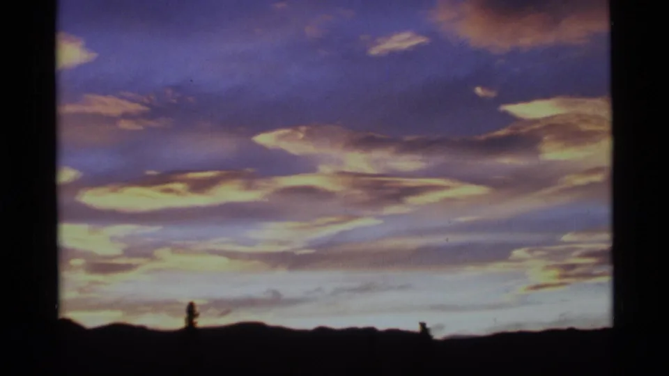 8mm Alaska frame from 1977 showing soft orange and yellow dawn clouds over a nearly black uneven horizon.