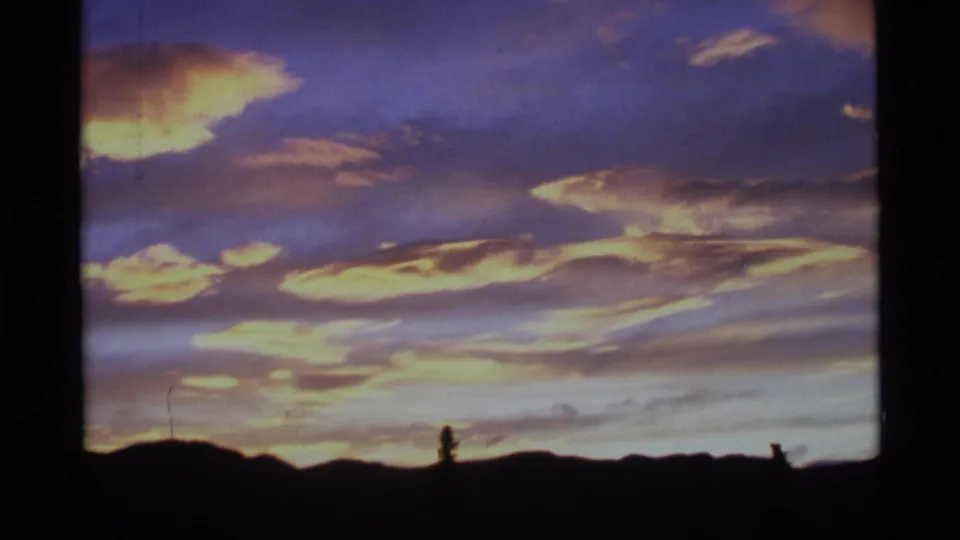 1977 Alaska 8mm still with orange dawn cloud patches, cool sky tones, and a black landscape silhouette below.