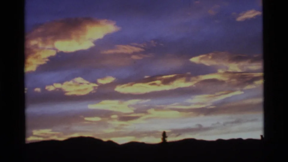 1977 Alaska 8mm frame showing purple and gold sunset clouds over a dark mountain ridgeline.