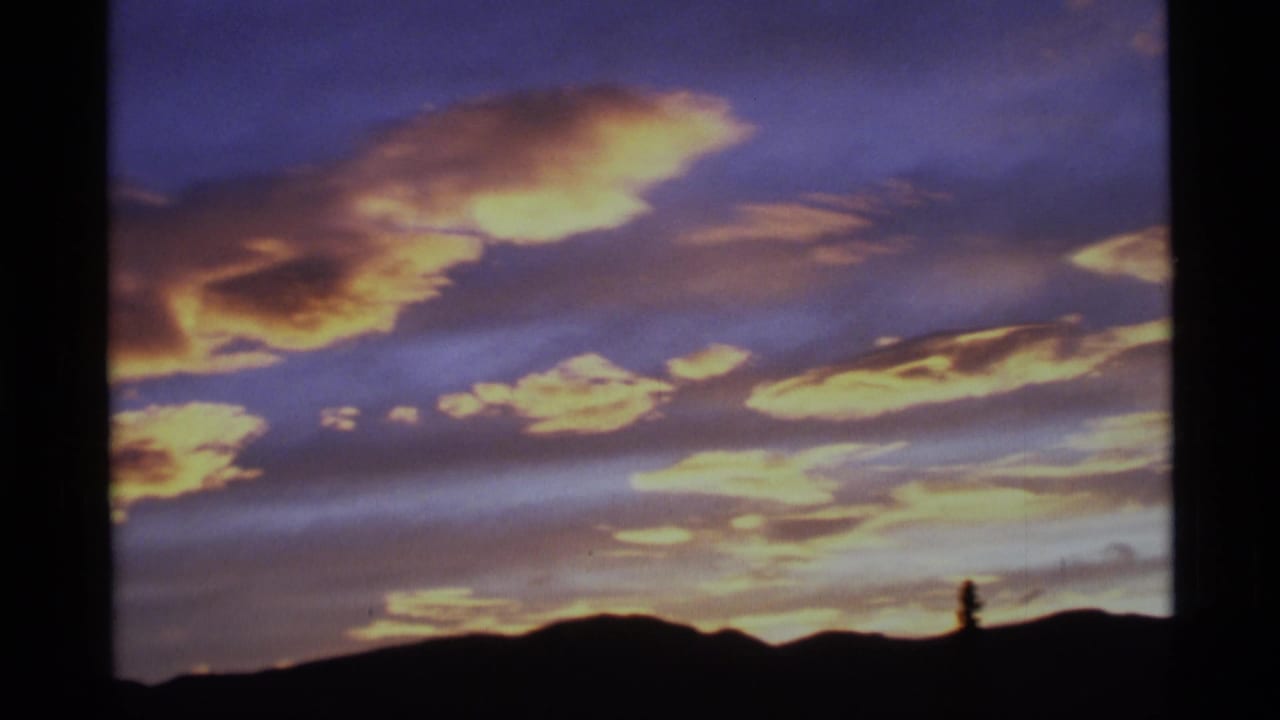 Alaska home-movie frame with saturated clouds and a silhouetted ridge under a purple evening sky.
