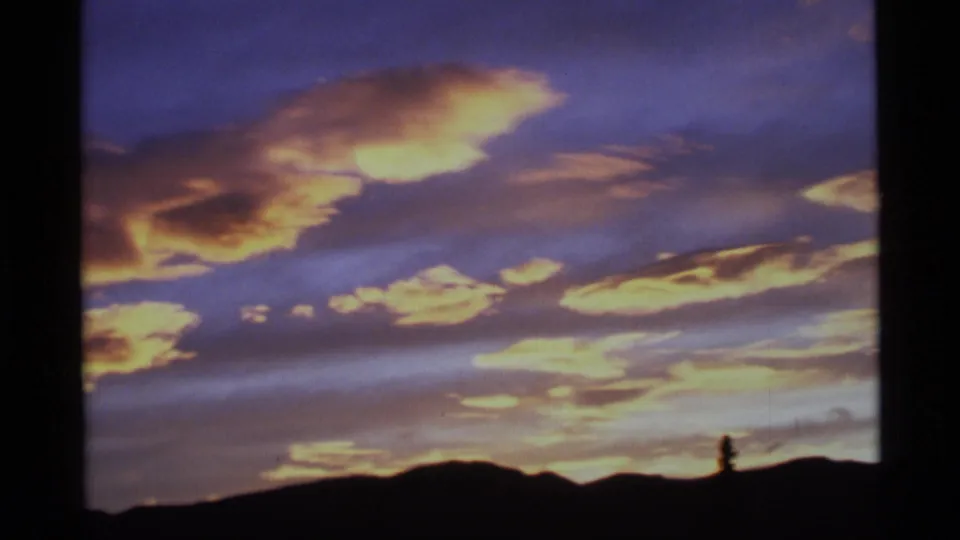 Alaska home-movie frame with saturated clouds and a silhouetted ridge under a purple evening sky.