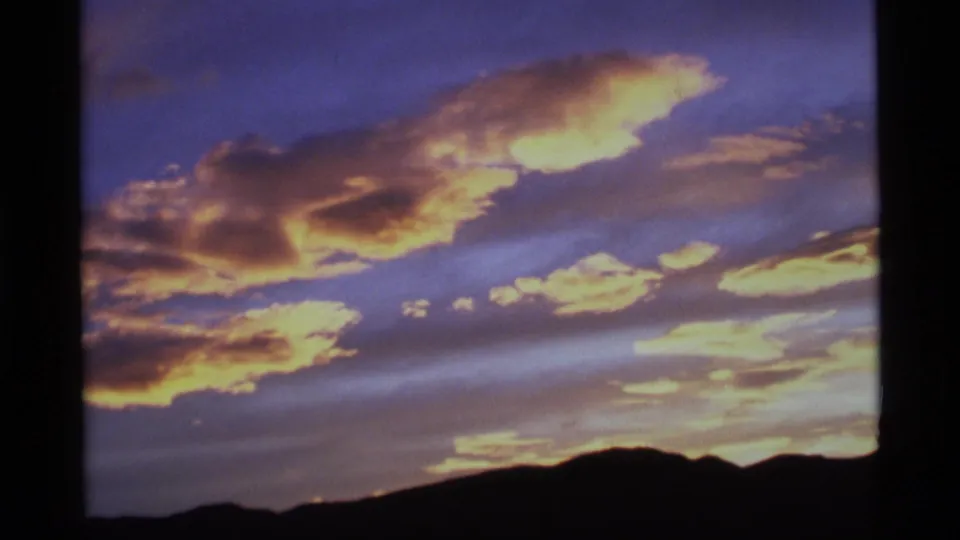 1977 Alaska 8mm view of warm sunset clouds and a dark mountain horizon, framed by visible film edges.