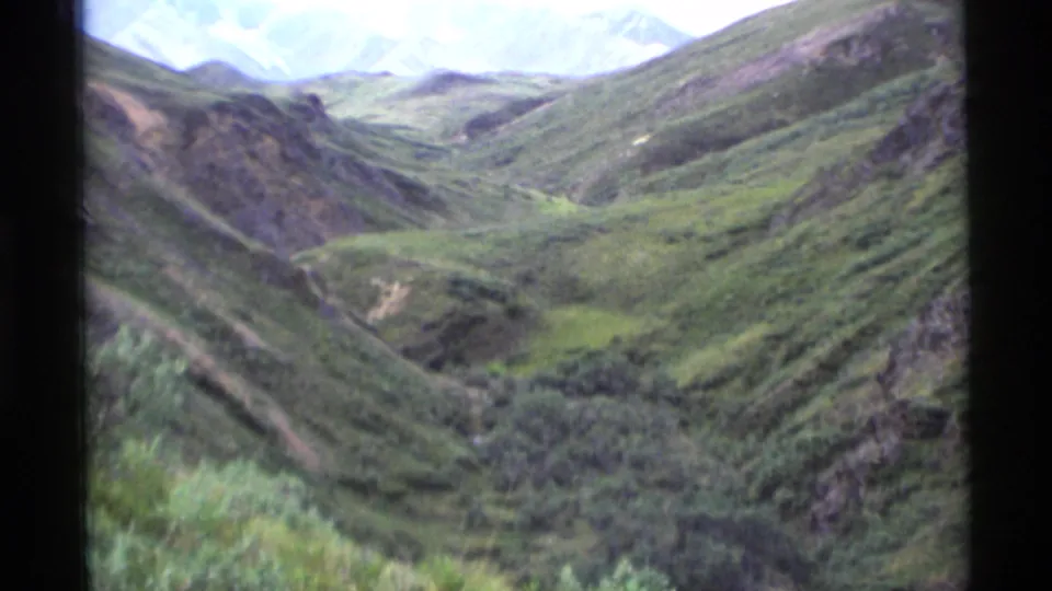 1977 Alaska 8mm view across a broad green valley framed by rugged slopes and distant high peaks.