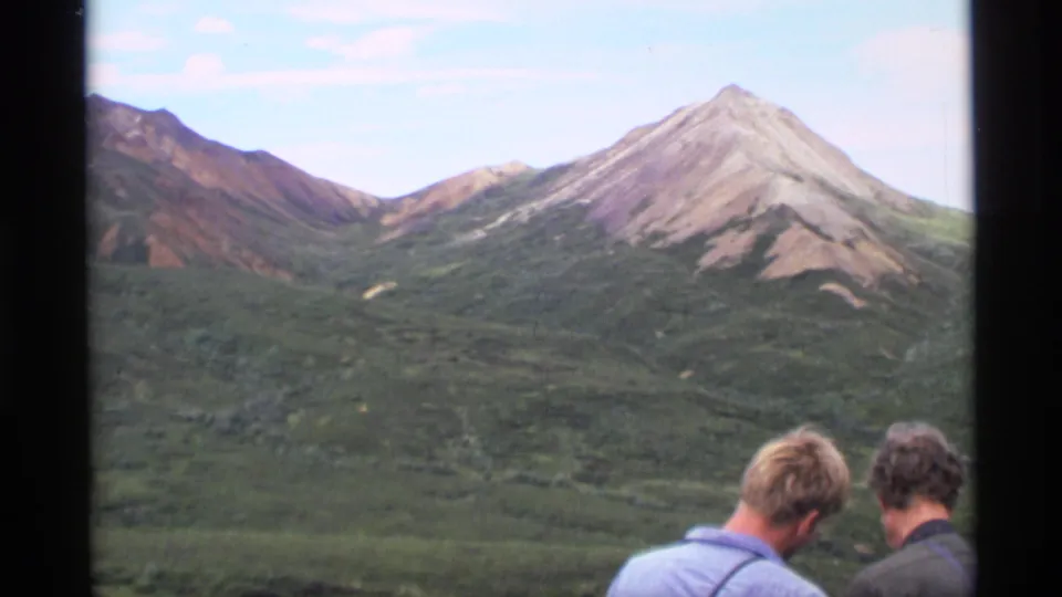 1977 Alaska 8mm frame with two people seen from behind facing a wide mountain vista.
