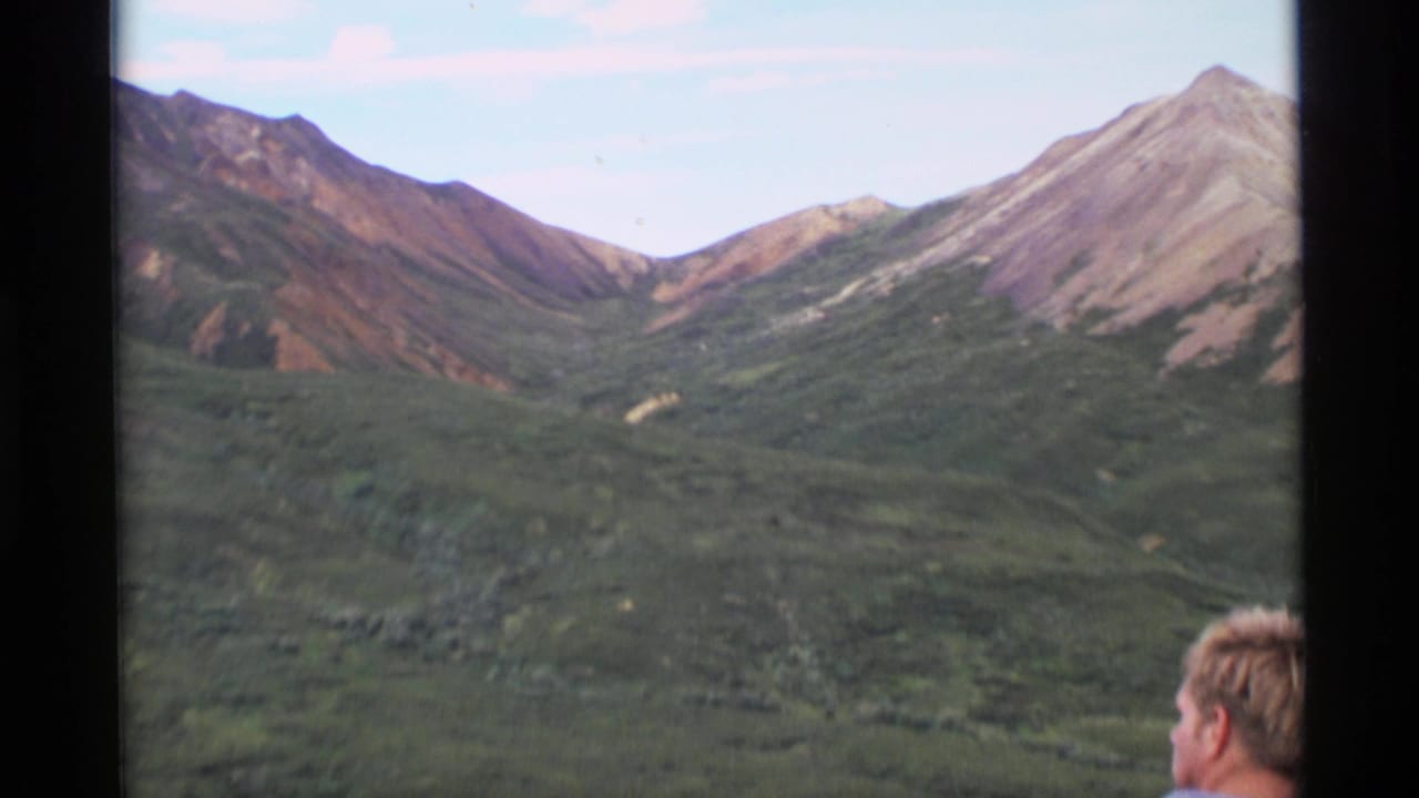 Mountain valley seen through dark film-frame borders with part of a person's head near the lower center.
