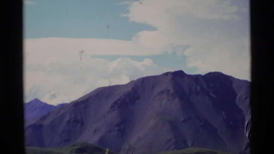 Soft 8mm view of an Alaska mountain ridge, with only the edge of a nearby hiker visible in frame.