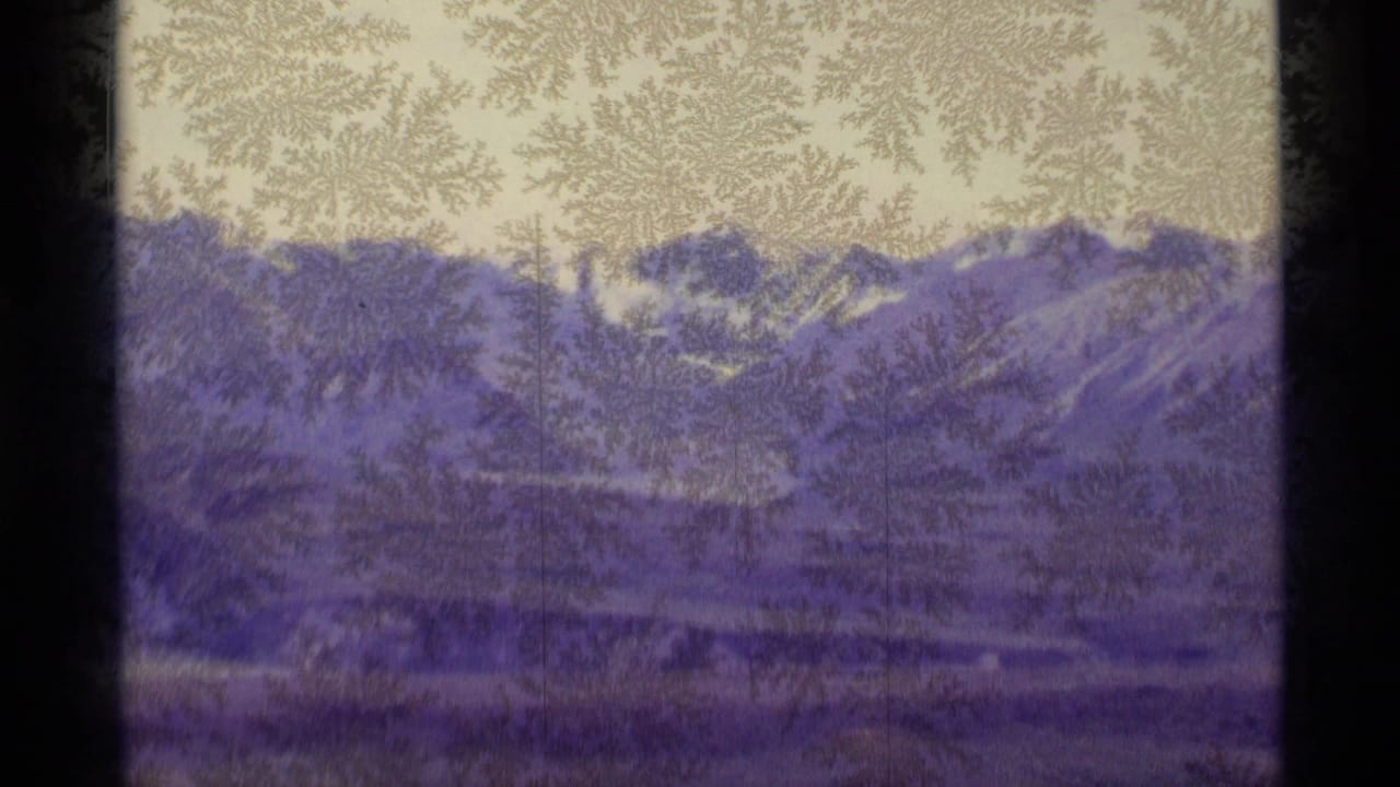 1977 Alaska 8mm frame showing frosted glass over distant snow-covered mountains, valley landforms, pale sky, and dark window edges.