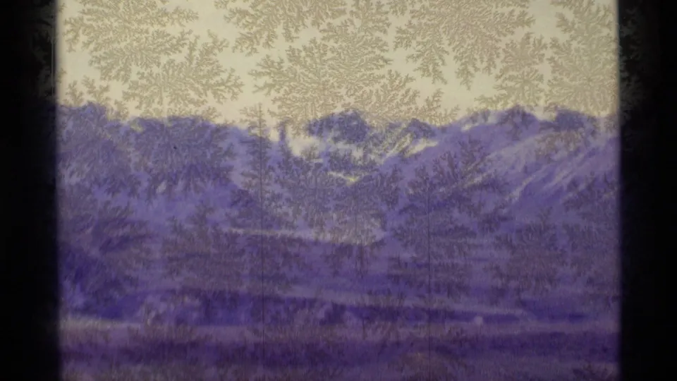 1977 Alaska 8mm frame showing frosted glass over distant snow-covered mountains, valley landforms, pale sky, and dark window edges.