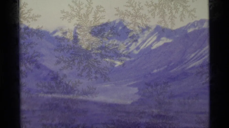 1977 Alaska 8mm frame showing a snow-covered peak and valley through frosted window glass, with visible grain and purple color shift.