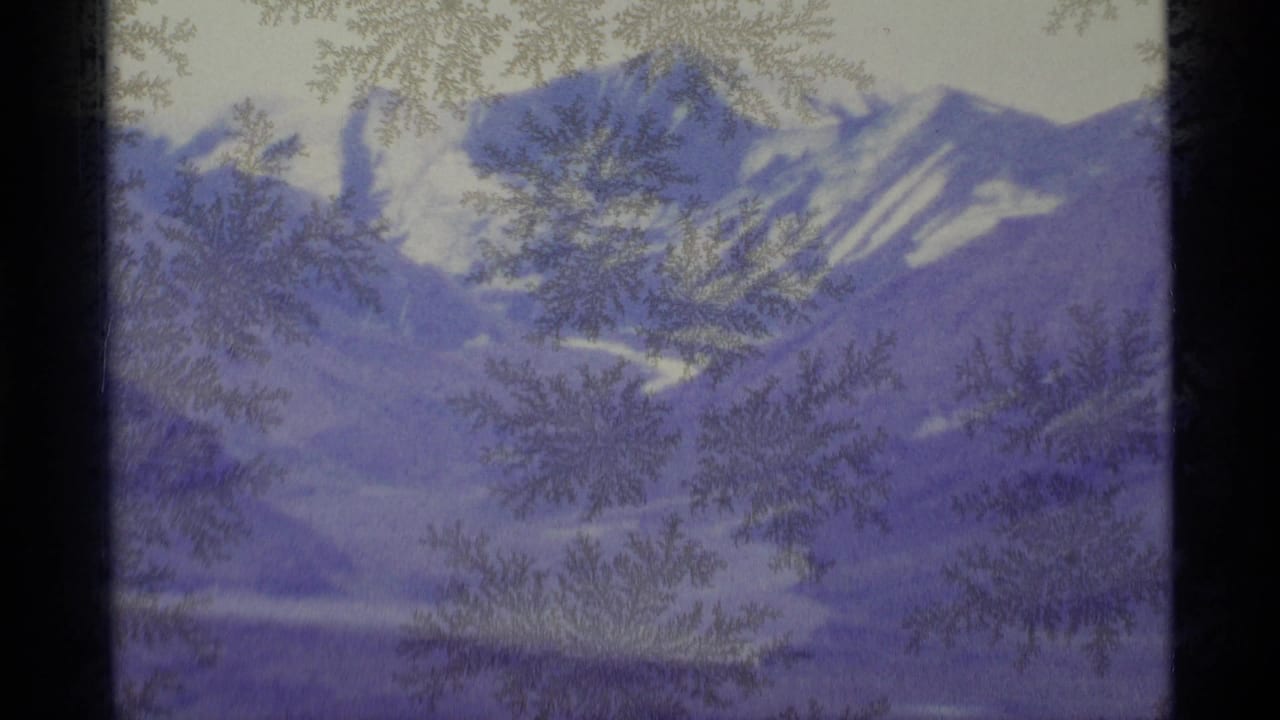 Snowy mountain range seen through frosty window glass with dark window edges.