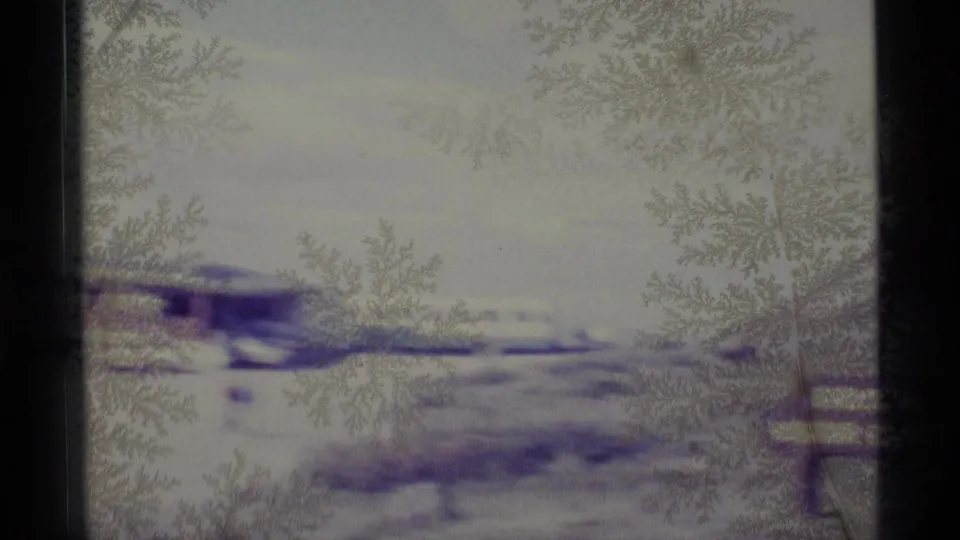 The final 1977 Alaska frame looks through icy glass toward a washed-out snowy scene, with a railing at the edge.