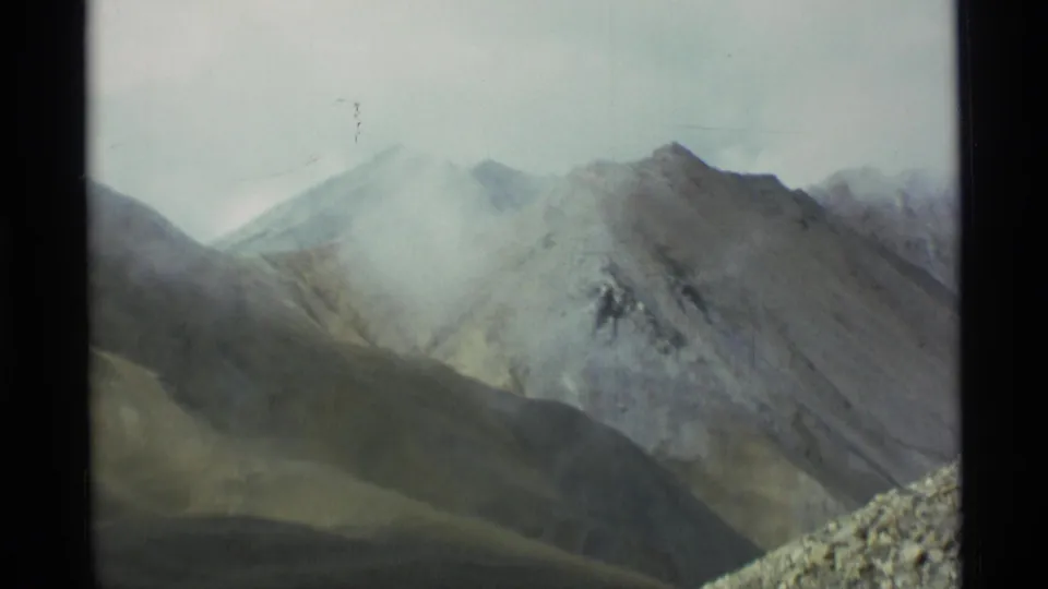 1977 Alaska 8mm frame looking toward barren ridges with fog moving across the slopes and a rocky foreground edge.