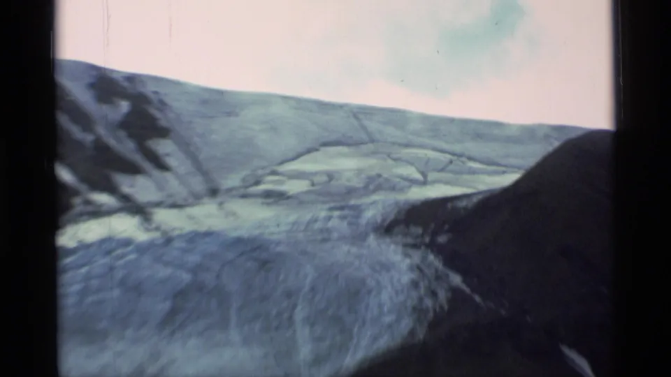 Closer 8mm view of glacier ice and rounded Alaskan mountain slopes, with soft focus, faded color, and handheld framing.