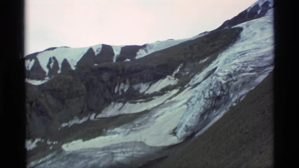 Alaska 1977 mountain view with glacier surface, shadowed rock faces, and uneven snowfields in a home-movie frame.