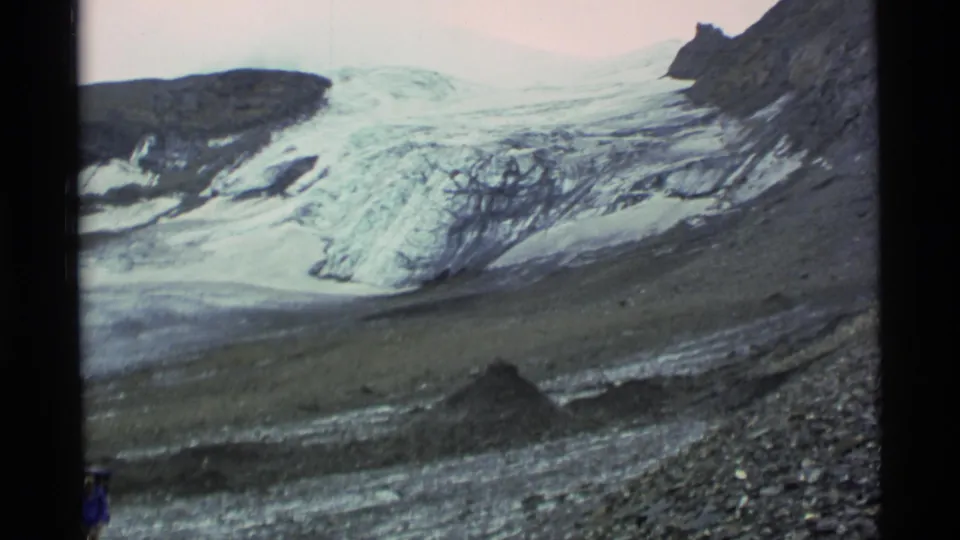 1977 Alaska 8mm frame with glacier ice and moraine terrain, with the hiker partly visible near the lower frame edge.
