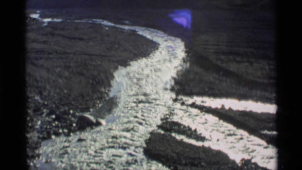 1977 Alaska 8mm frame showing a bright winding river cutting through a rugged valley with dark slopes around it.