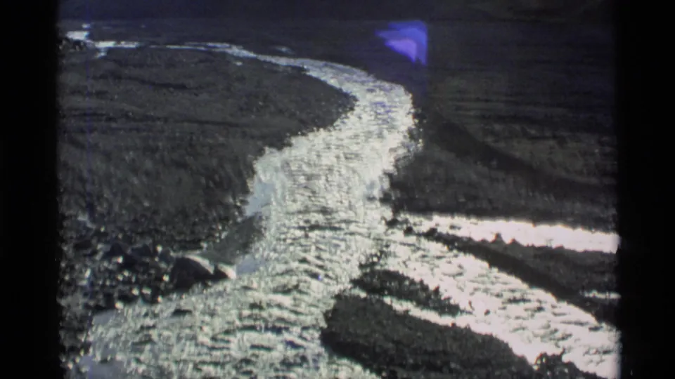 1977 Alaska 8mm frame showing a bright winding river cutting through a rugged valley with dark slopes around it.