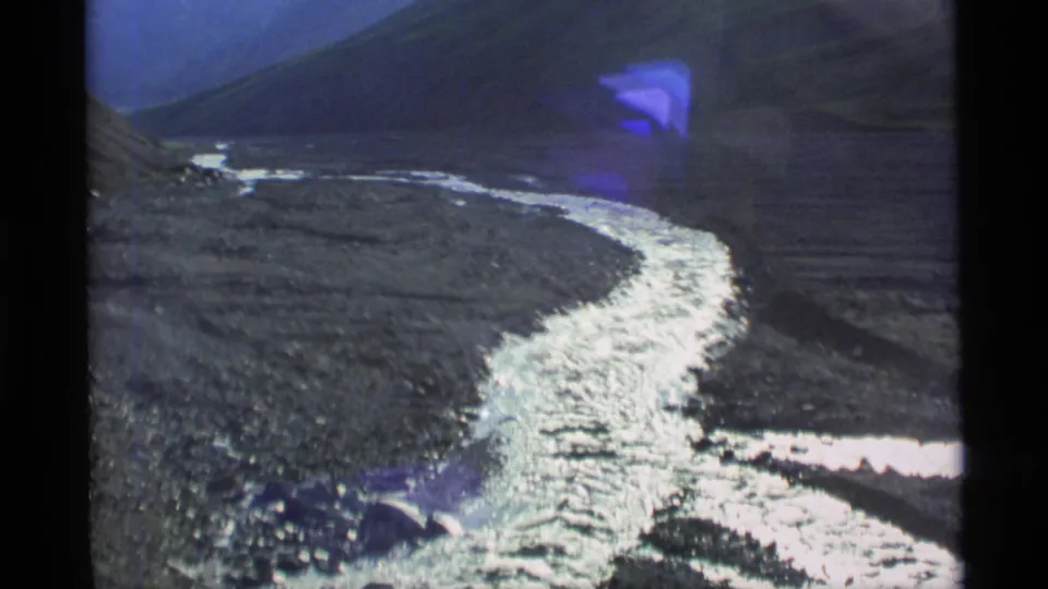 1977 Alaska 8mm frame with a silvery river running away through a broad, rugged valley under a darker hillside.